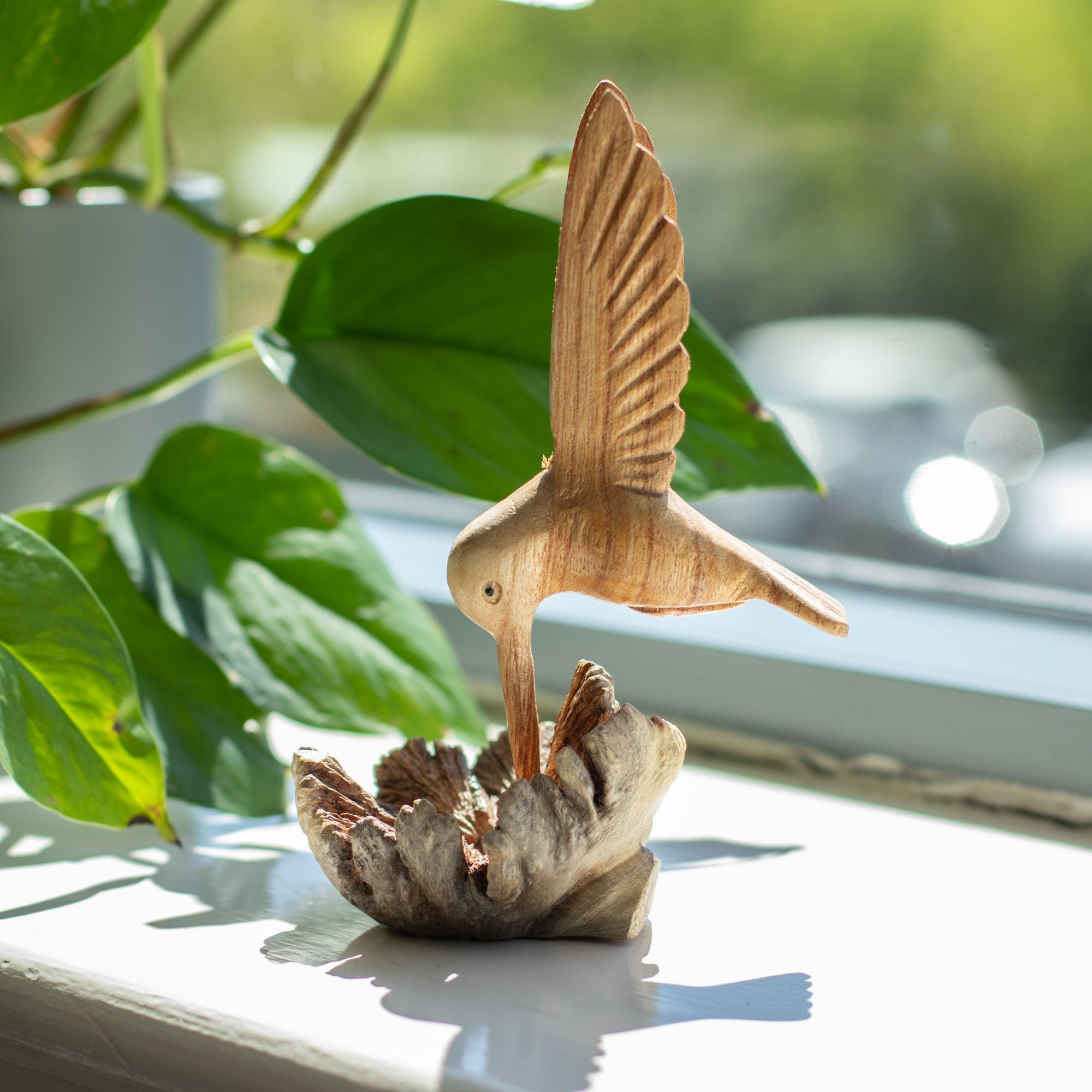 Rankų darbo kolibro skulptūra, geriančio nektarą iš medžio išaugos