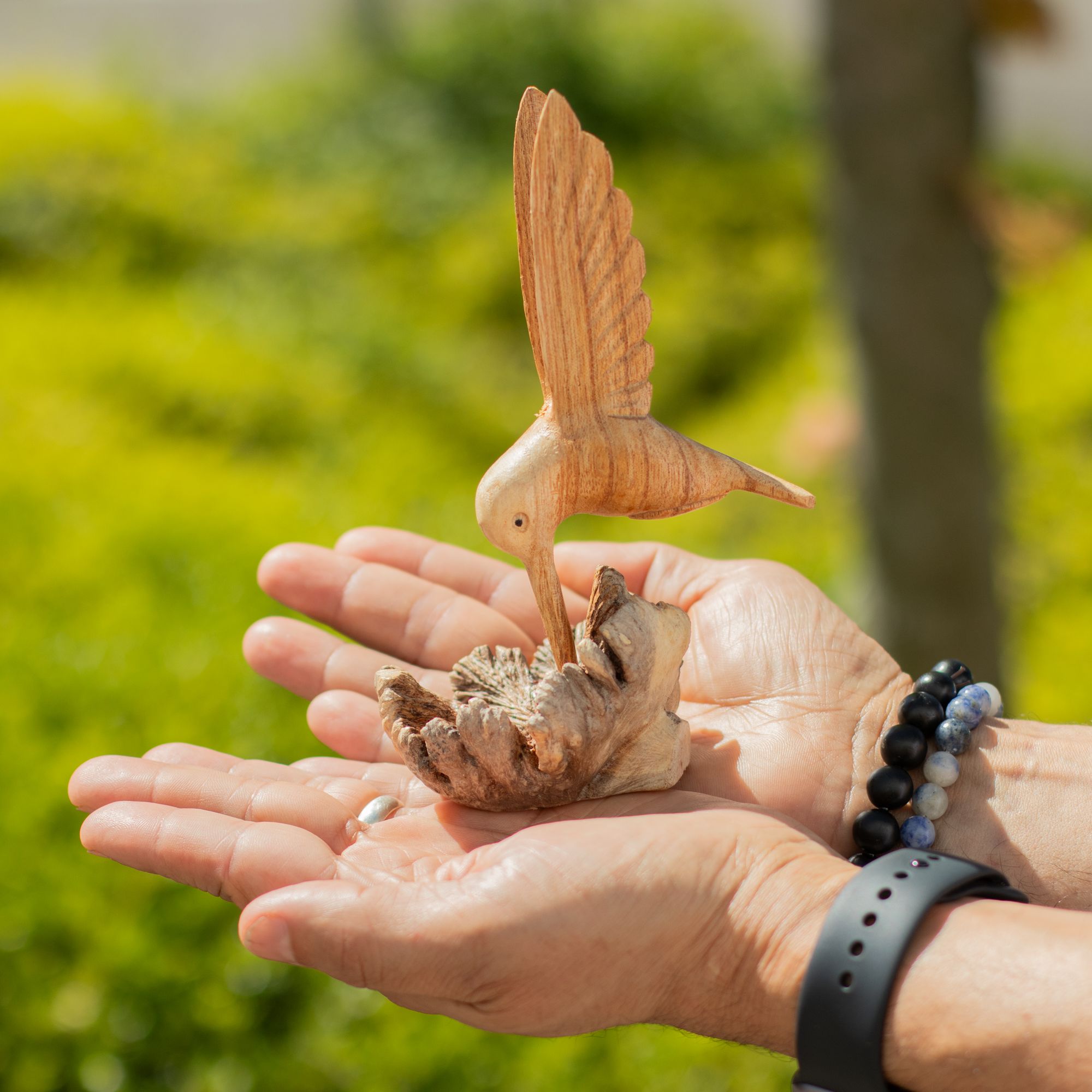 Rankų darbo kolibro skulptūra, geriančio nektarą iš medžio išaugos